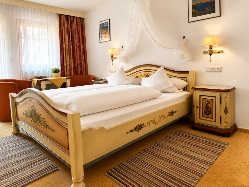 Painted double bed with a white canopy, bedside table with floral decoration, striped rugs and armchairs by the window