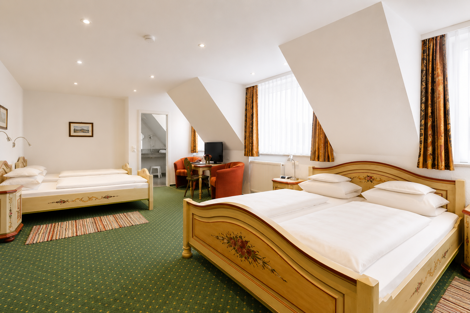 Family room with a double bed and two single beds in light painted wood, green carpeting, armchairs and a sloping ceiling
