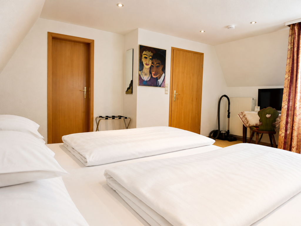 Double bed with white bed linen, doors, a painting on the wall and a desk with a TV in the background