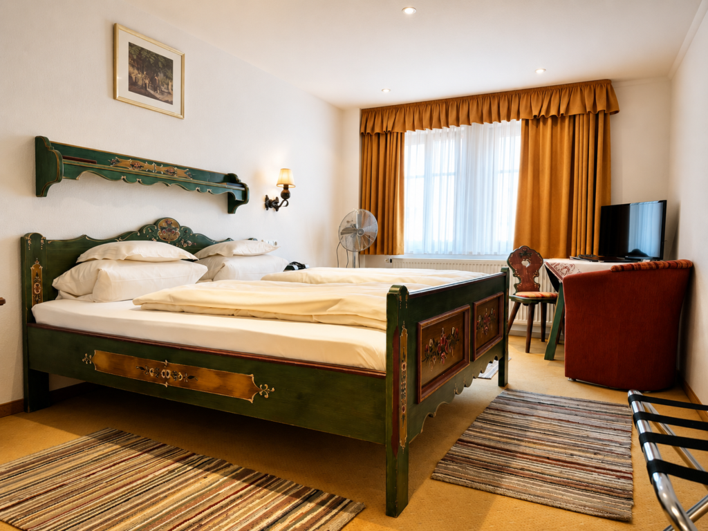 Green-painted double bed with a wall shelf, behind it a window, a desk with a flat-screen TV and a red armchair