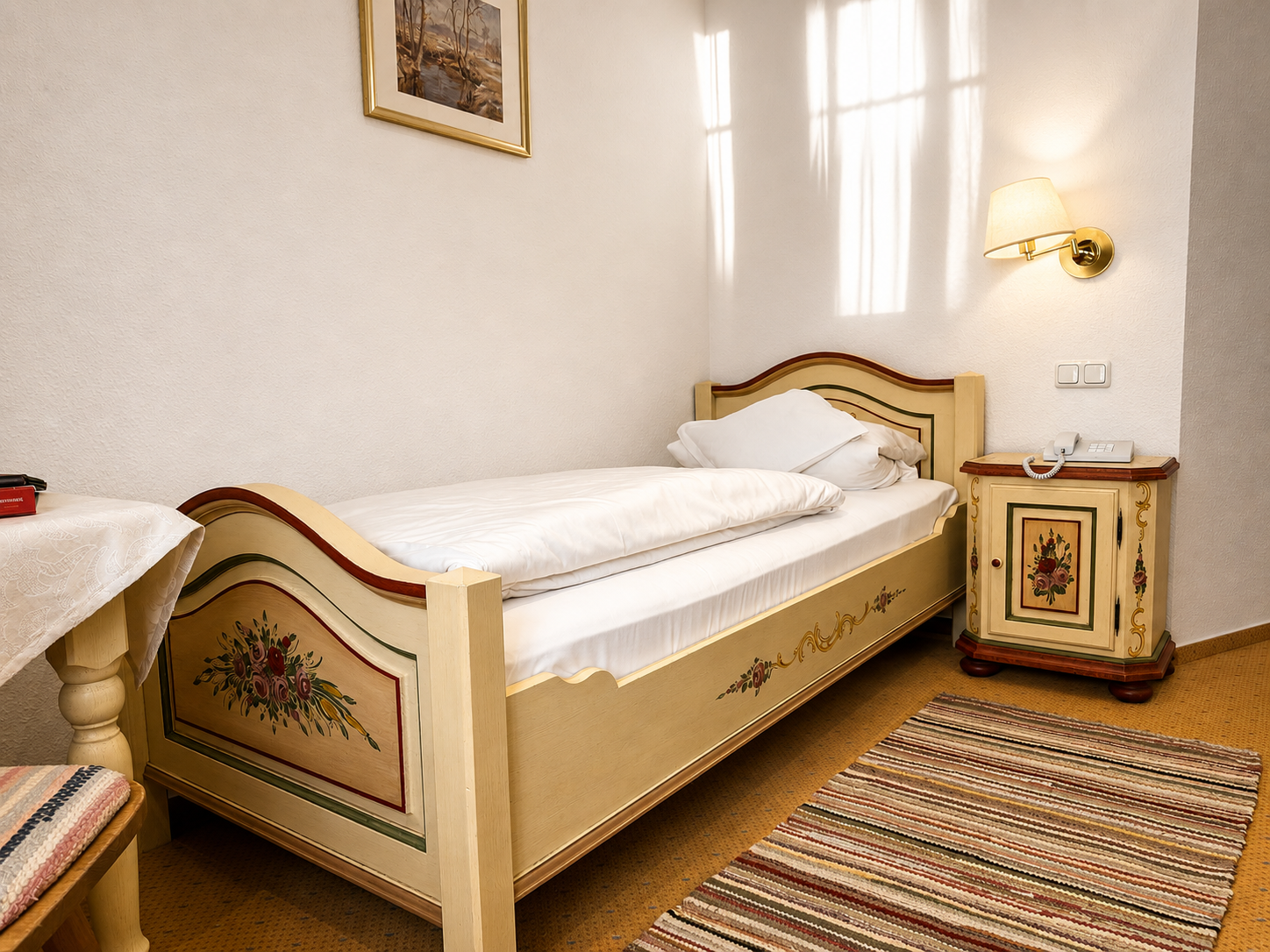 Single Room with a cream hand-painted farmhouse bed decorated with flowers, a painted bedside table, wall light and woven rug