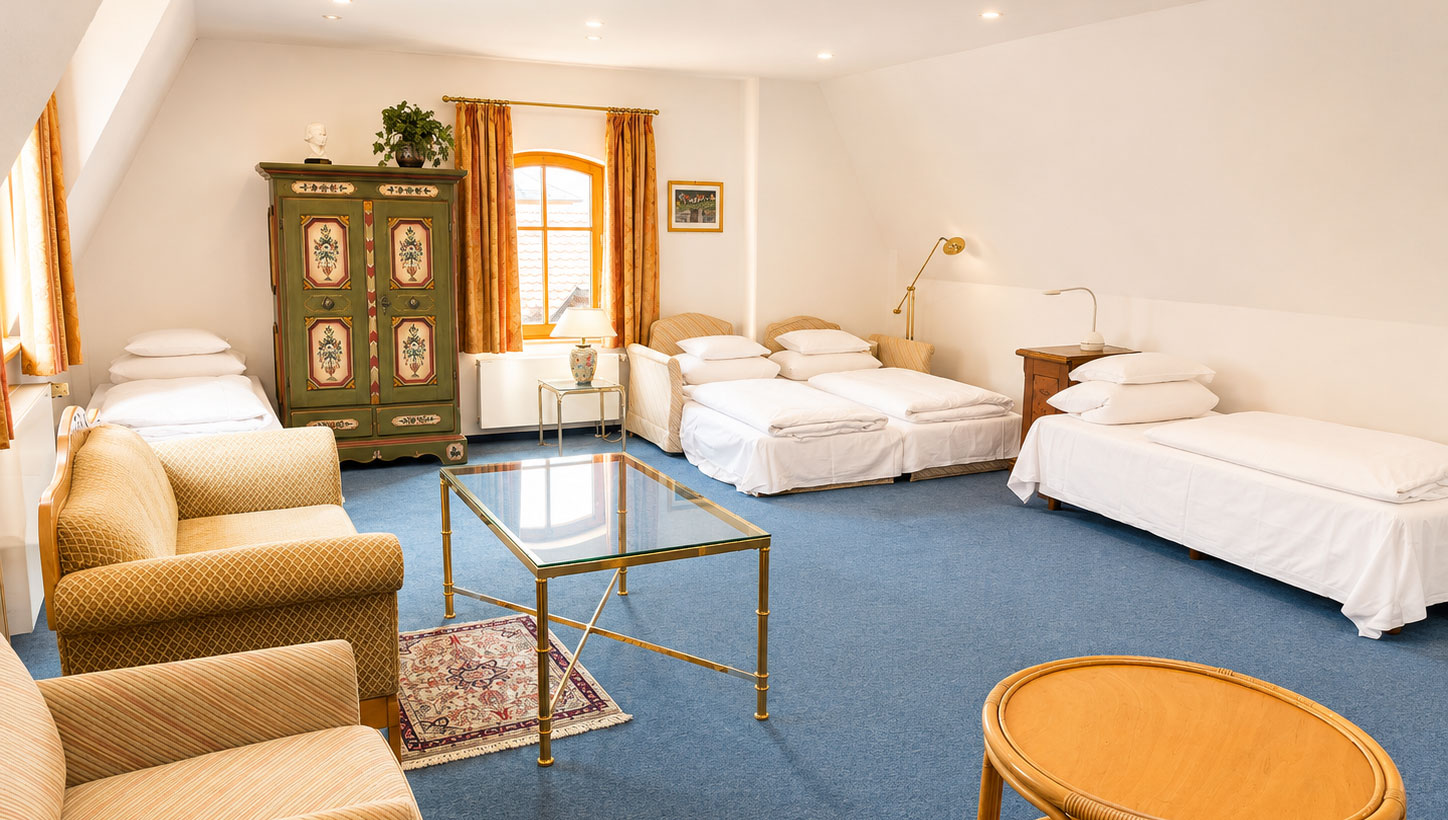 Large room with single beds, a painted green farmhouse wardrobe, upholstered armchairs and a glass table on blue carpeting