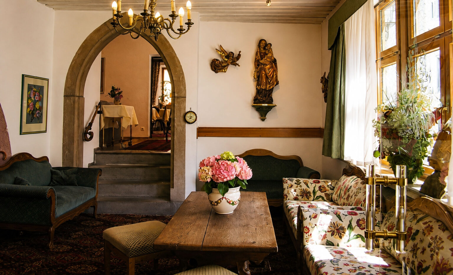 Hotel lounge with a pointed arch, a carved Madonna and Child and an angel on the wall, green sofas and hydrangeas