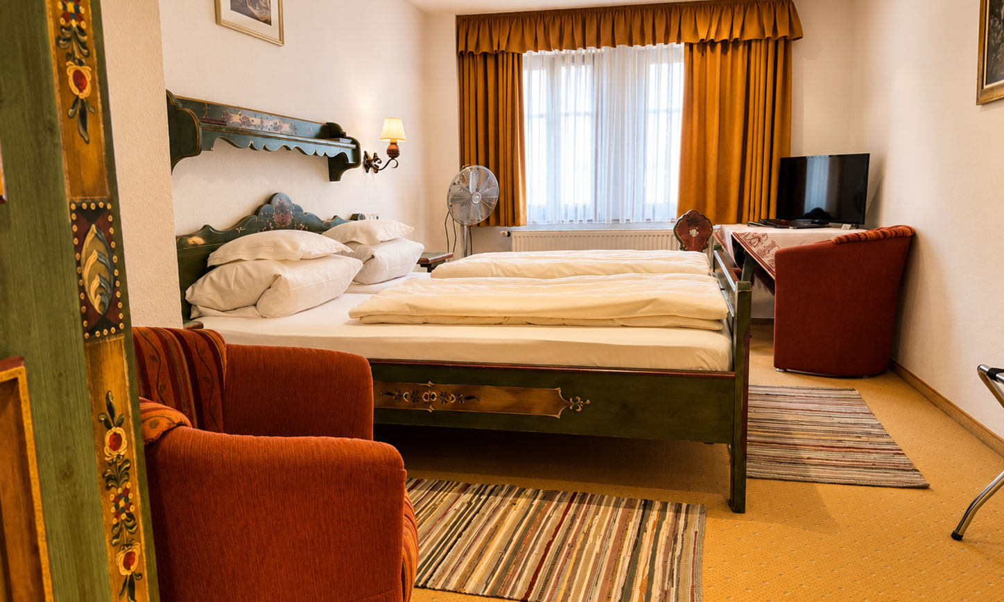 Double Room with a green-painted farmhouse bed, a red armchair, a wall light and a window with golden curtains