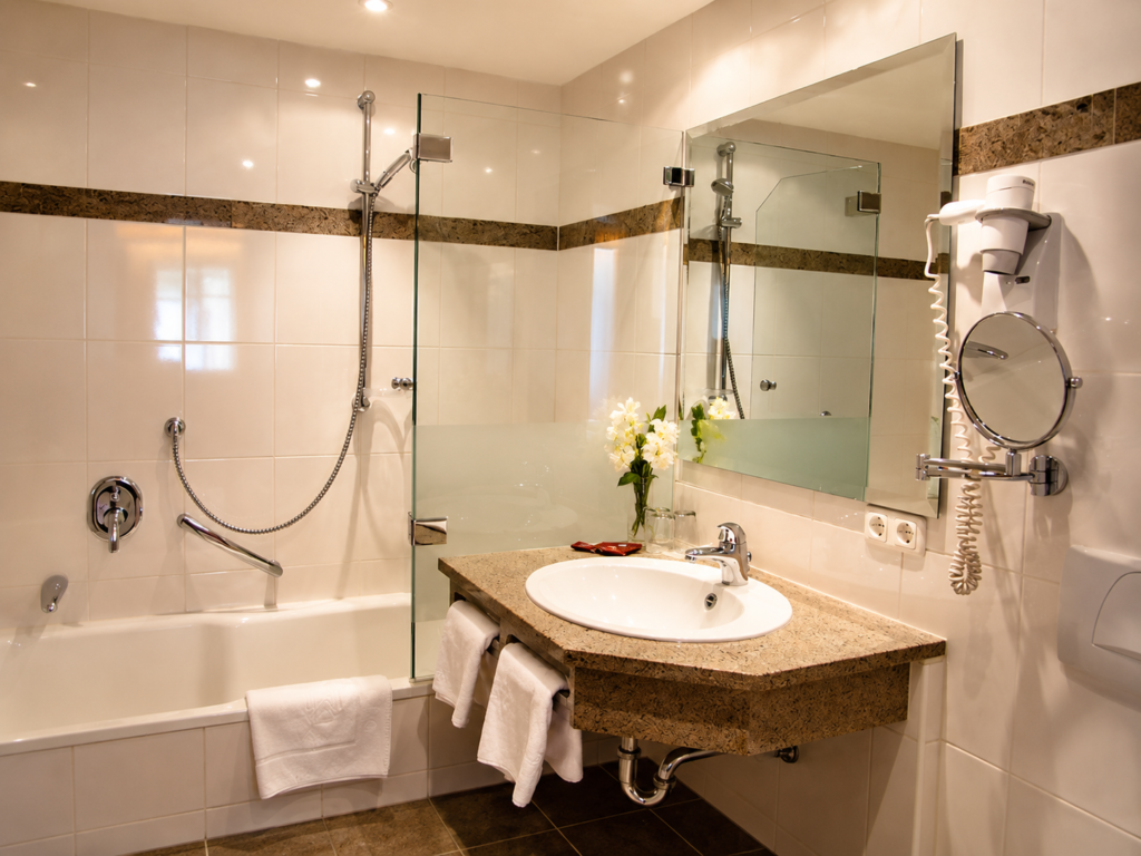 Bathroom with light tiles, washbasin, mirror, bath with a glass screen and towels