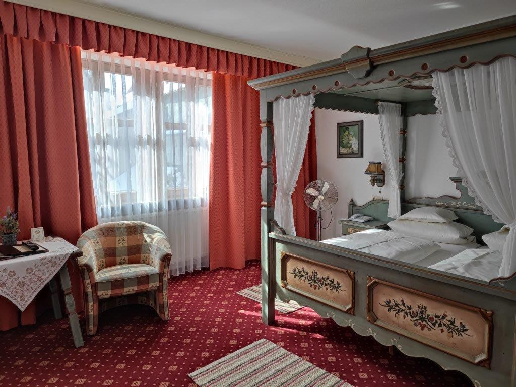 Room with a four-poster bed, a patterned armchair by the window, red curtains and red carpeting