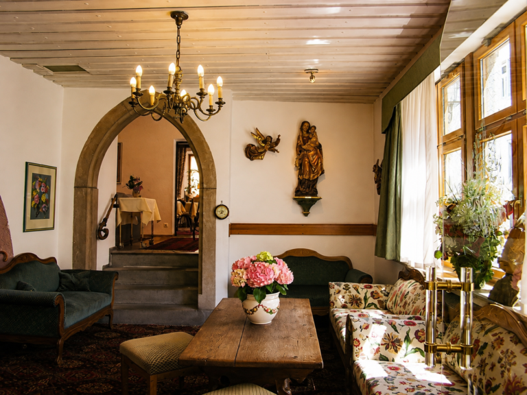 Stube mit Rundbogen, geschnitzter Heiligenfigur an der Wand, Holztisch und Blumen