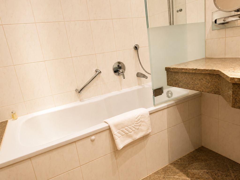 Badezimmer mit Badewanne, Glasabtrennung, Handtuch und Waschtisch aus Stein