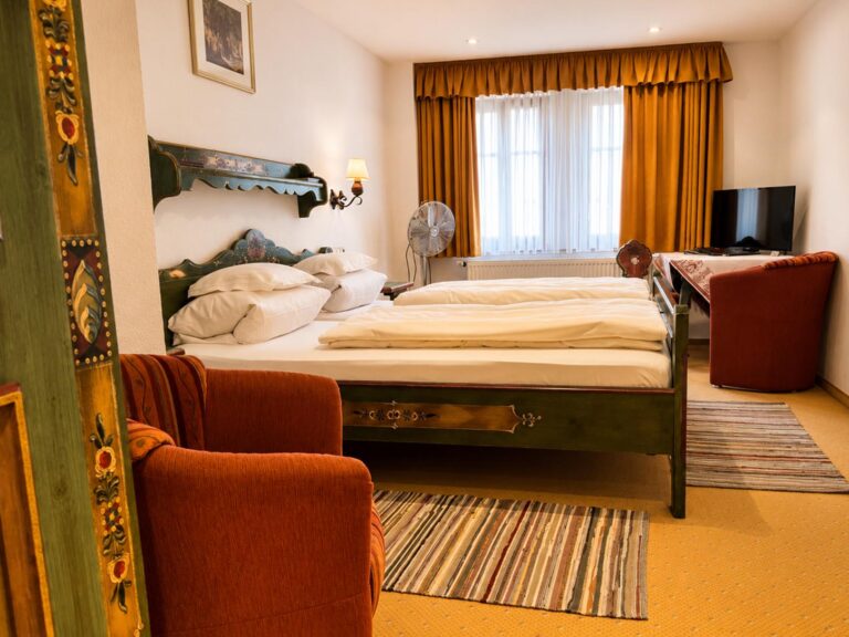 Double Room with a green painted double bed, red armchair and bright windows