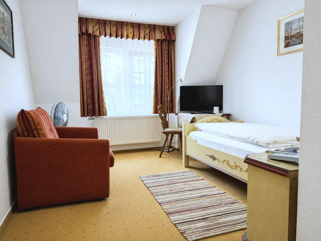 Single Room with a red armchair, a window with curtains, a desk with a flat-screen TV and a single bed