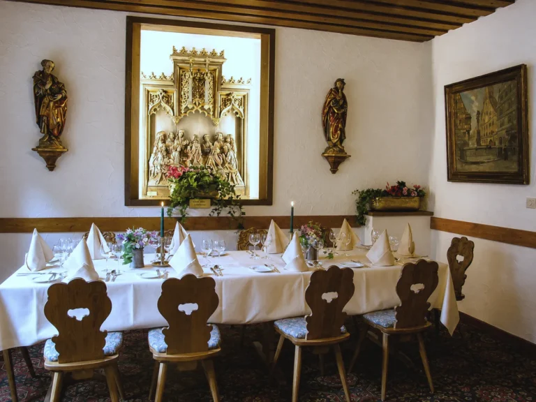 Gedeckte Tafel in einer Stube vor einem geschnitzten Flügelaltar, links und rechts zwei Holzfiguren