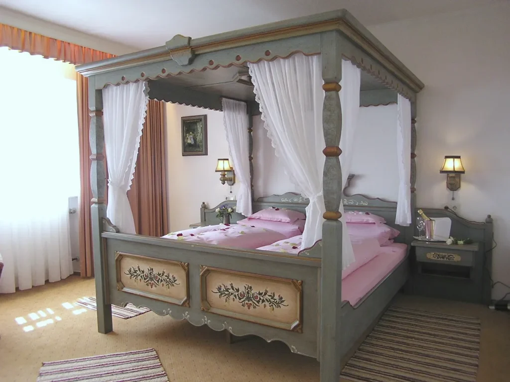 Four-poster bed with hand-painted panels at the foot end, white curtains, pink bed linen and wall lights