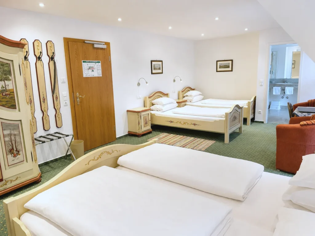 View across the double bed to two painted single beds, a farmhouse wardrobe with a coat rack, a wooden door and the open bathroom door
