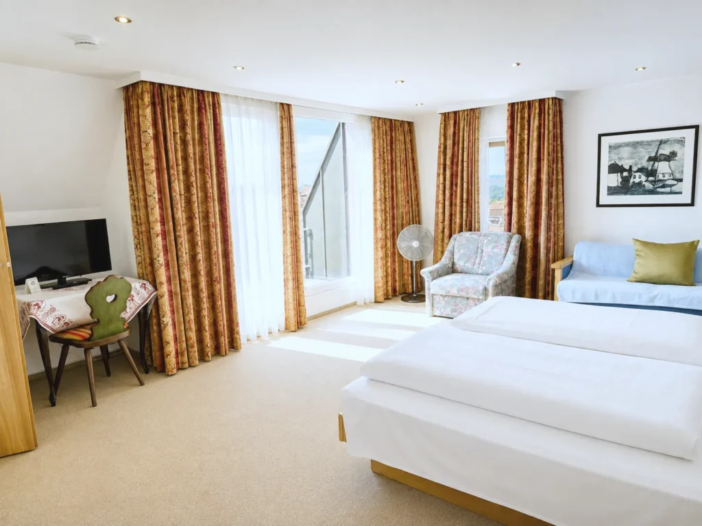Bedroom with a double bed, sofa bed, armchair, desk with a TV and a door to the balcony