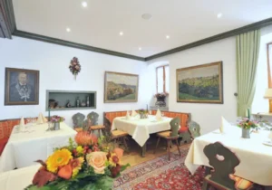 Tiroler Stube mit gedeckten Tischen, gepolsterter Eckbank und Gemälden an der Wand